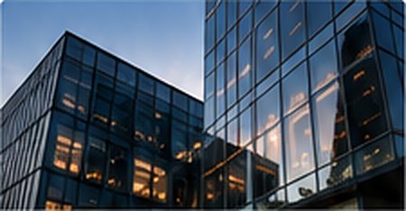 Glass office towers reflecting a sunset sky